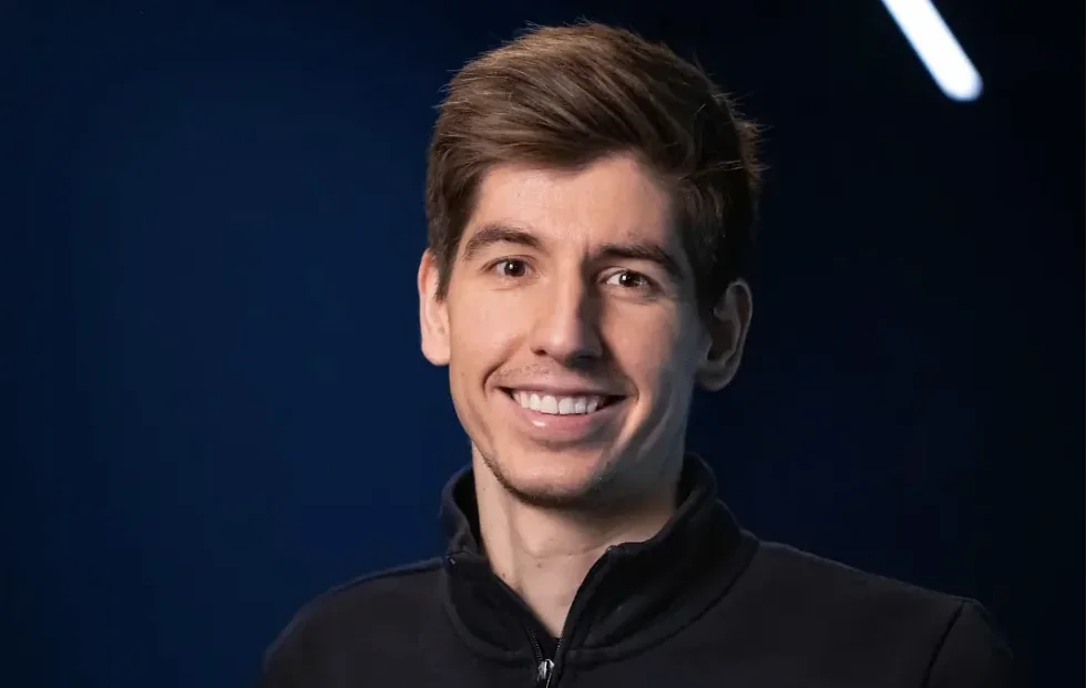 Diogo Oliveira smiling in a portrait lit against a deep blue background.