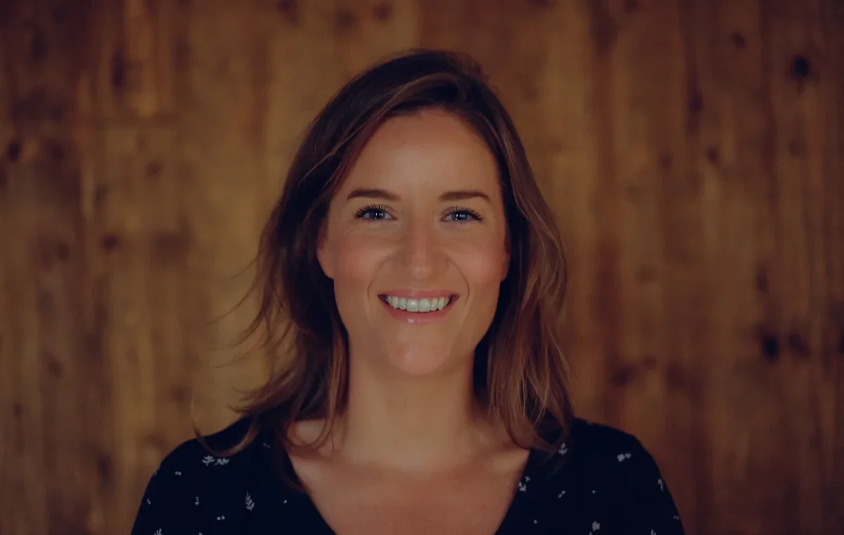 Lesley Tully smiling in a portrait against a warm wood-panelled wall.